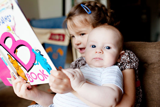 A toddler reads an ABC book to her baby brother