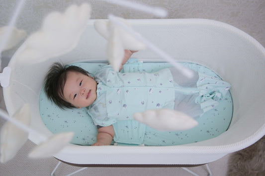Baby gazes up from SNOO at Sky, a cloud baby mobile from Happiest Baby