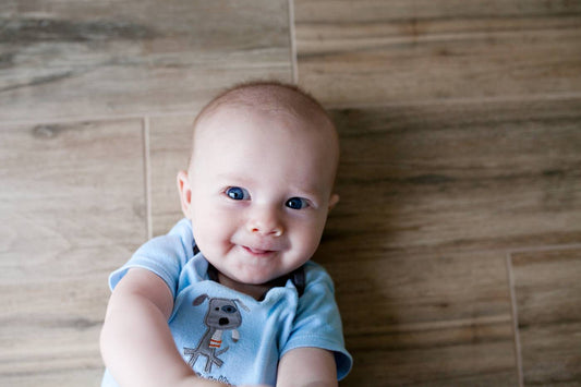 Baby in blue laying on floor smiling