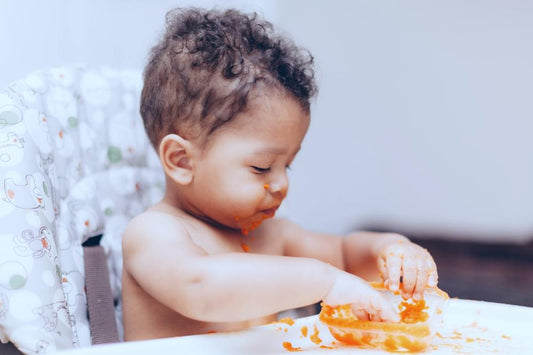 Baby in a high chair eating orange pureed baby food