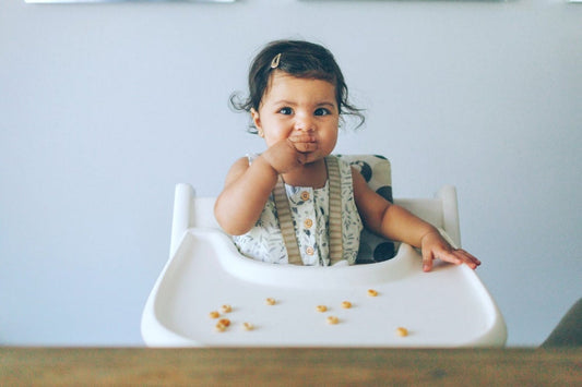 Baby girl eats finger food in a highchair