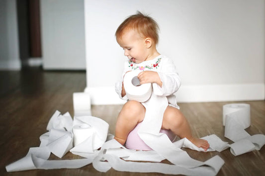 A toddler girl unravels toilet paper rolls