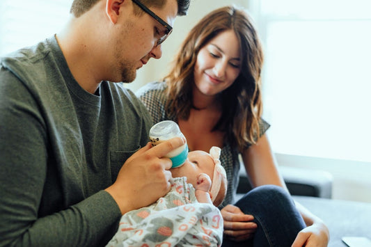 A father bottle-feeds his newborn baby as the mother watches