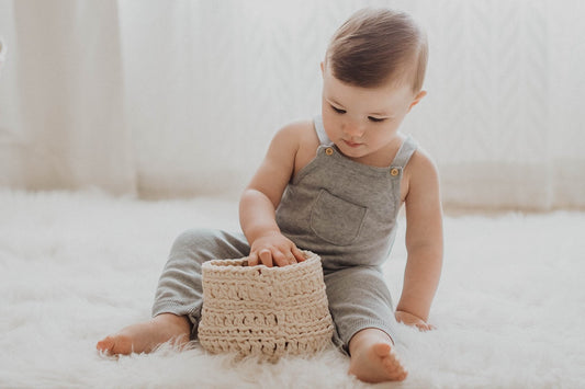 A baby explores a basket on the floor.