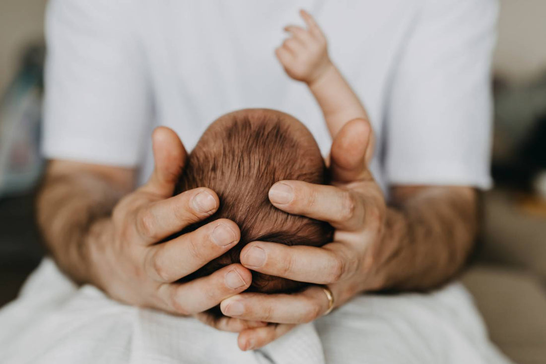 A father cradles his newborn's head in his hands.