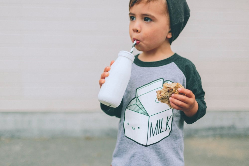 Toddler drinks milk while wearing a shirt that says "milk"