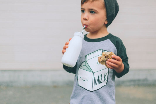 Toddler drinks milk while wearing a shirt that says "milk"