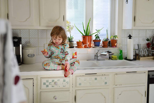 A toddler girl sits on the kitchen counter and eats a snack in her pyjamas