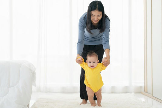 A baby is learning to walk with help from her mom