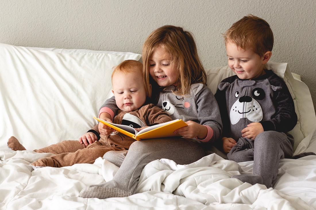 Books about friendship - two toddlers and a baby reading together on a bed