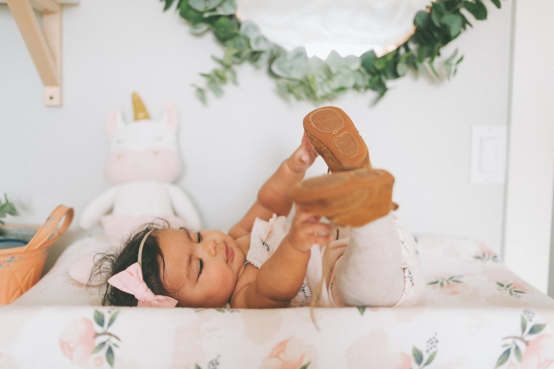Cute baby girl laying on changing table grabbing at her feet. 