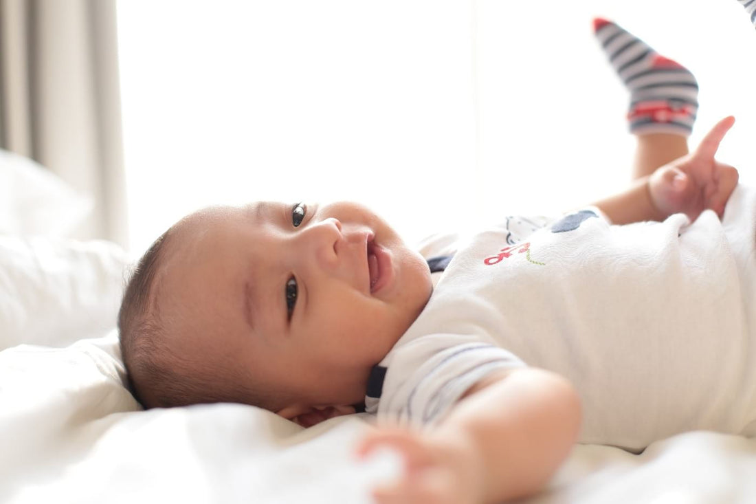 Baby laying on his back on a bed and smiling.