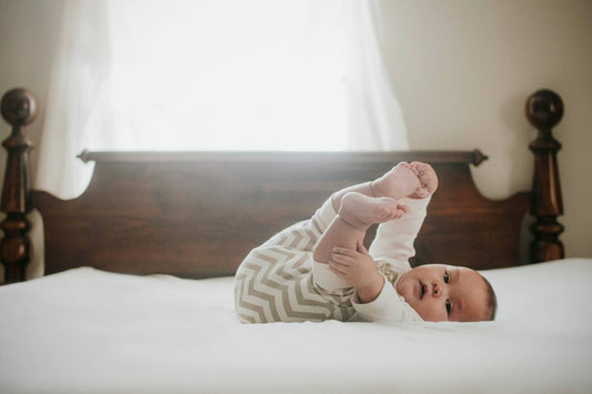 A baby lays on their back and grabs their toes