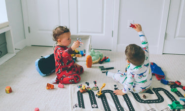 Two toddler boys play on the carpet with cars and a road rug
