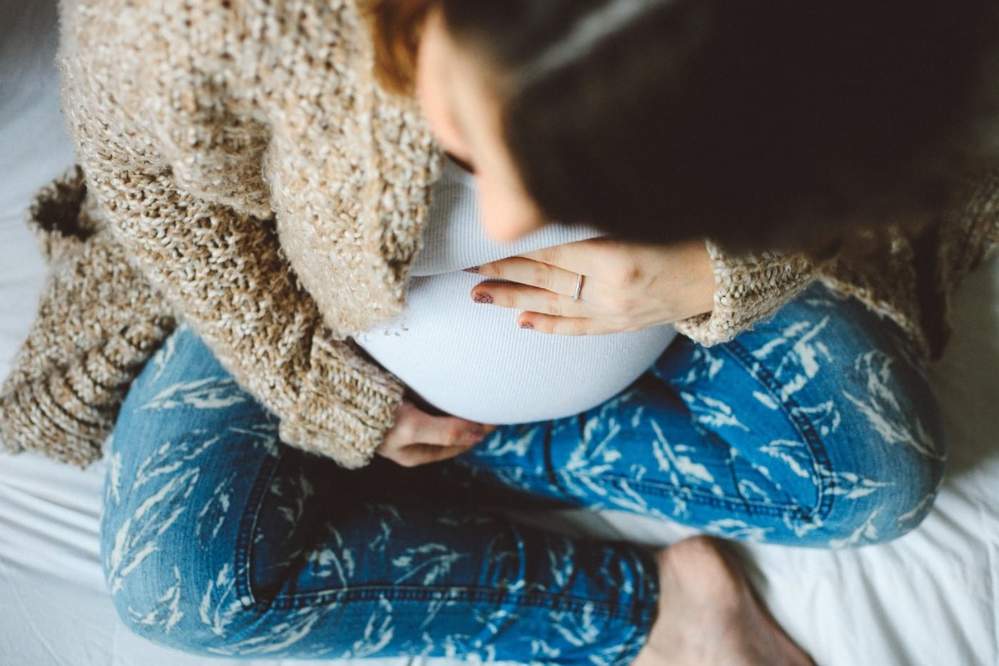 A pregnant woman sits cross-legged as she cradles her belly