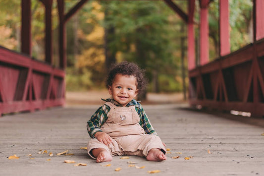 Baby boy sits on a bridge with fall foliage in the background