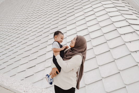 Mother in head scarf holding and smiling at toddler son.