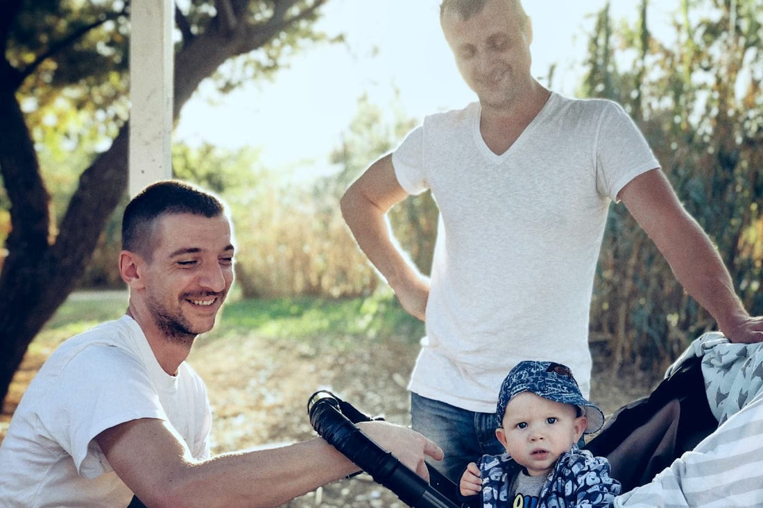 two dads and their baby in a stroller on a walk 