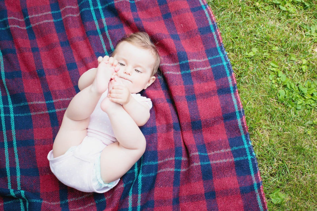 Baby girl laying on tartan blanket and grabbing at her feet.