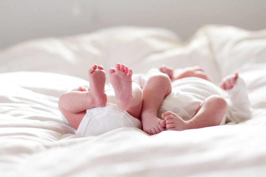 Twin babies laying on a bed.