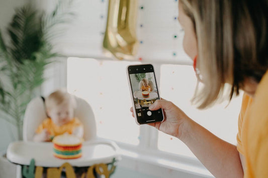 Mom uses a phone to record a video of a baby with a smash cake to celebrate a first birthday