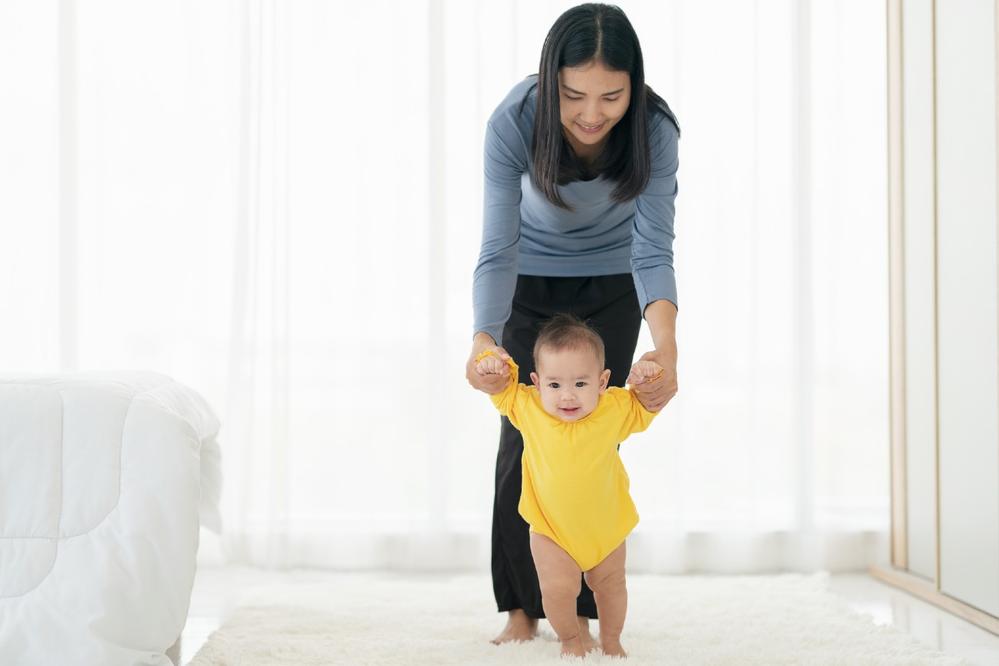 A baby is learning to walk with help from her mom